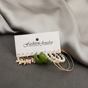 Macro view of 5-piece earring set with gold butterfly charms and pearls on white card