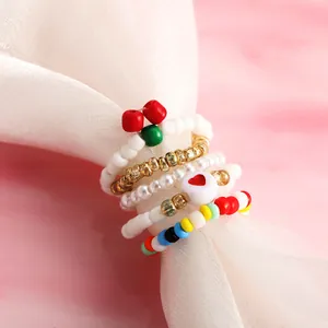 Dettaglio del set di anelli di perline colorate con ciondoli a cuore e ciliegia su tessuto