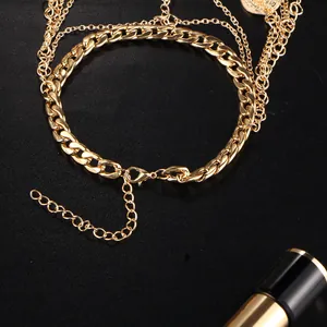 Détail de la chevillère dorée multicouche avec pendentif pièce vintage et fermoir mousqueton