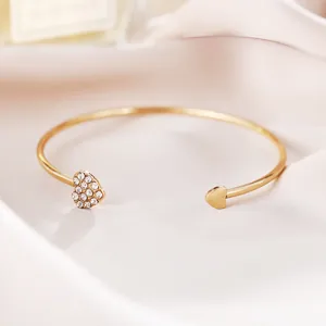 Detail van een goud vergulde hartarmband met pavé kristallen op een satijnen achtergrond