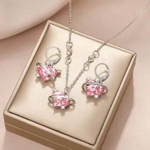 Détail d'une parure bijoux cœur rose et design saturne avec boîte dorée élégante