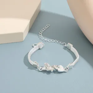 Detalle de pulsera de malla plateada con dijes de mariposa y corazón con cristales