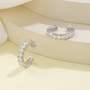 Macro shot of silver ear bone clips with sparkling round zircons on beige stand