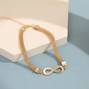 Detalle del dije de infinito con diamantes en tobillera dorada de tres capas con cierre