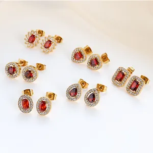 Macro detail of various gold and red zircon stud earrings on elegant white satin fabric