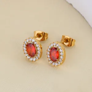 Close-up of golden earrings with red oval zircon and white stone halo accents