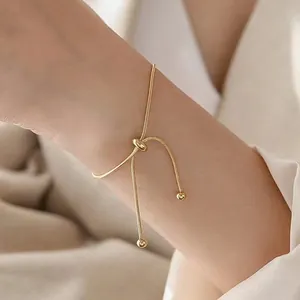 Detail of adjustable gold snake chain bracelet with spherical beads on white fabric