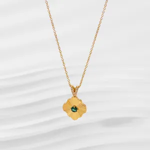 Macro view of gold flower pendant with green gem and zircon-set bail on a fine chain