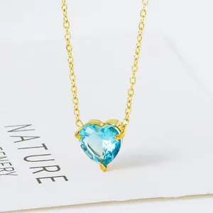 Macro-opname van een gouden hartketting met gefacetteerde blauwe zirkoon hanger op wit