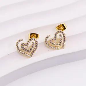 Detail shot of heart-shaped gold stud earrings with cubic zirconia on white pedestal