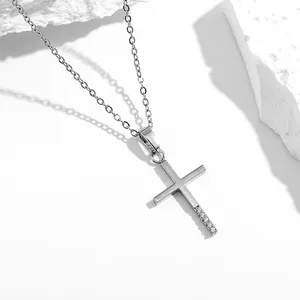 Detalle de un collar con colgante de cruz plateada con cinco circonitas sobre piedra blanca