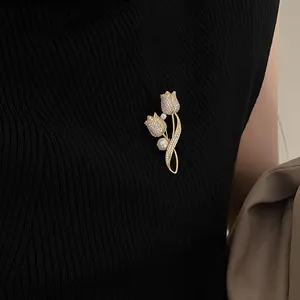 Elegante broche de tulipán dorado con cristales brillantes y perla blanca sobre tela negra