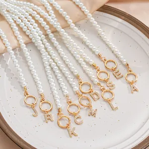 Close-up of pearl necklaces with gold OT buckles and rhinestone alphabet pendants in a tray