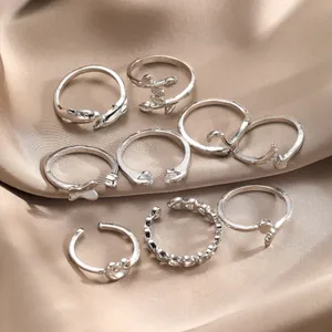 Set of 8 silver boho rings featuring heart, leaf, and butterfly motifs on champagne satin