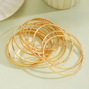 Dettaglio di bracciali rigidi boho dorati sovrapposti con superfici lucide e intrecciate