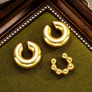Detailed view of three polished gold C-shaped ear cuffs on dark textured fabric