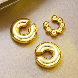 Macro detail of three gold-plated C-shaped ear cuffs with smooth and beaded metal textures