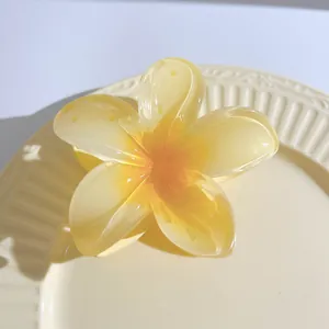 Detailed view of 7cm translucent frangipani flower hair claw on a ceramic plate