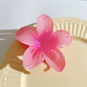 Detail of pink gradient frangipani flower hair claw clip on a textured beige ceramic plate