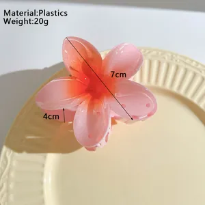 7cm floral hair claw clip with orange-pink gradient finish on a textured ceramic dish
