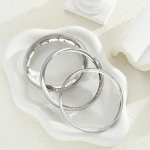 Set di tre bracciali minimalisti in metallo argento impilabili su un piatto decorativo