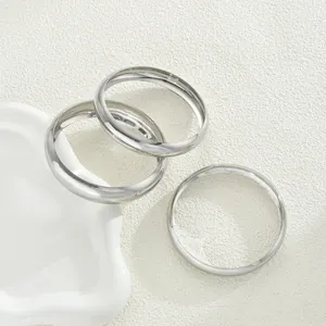 Tre bracciali rigidi argentati lucidi minimalisti su una superficie bianca testurizzata