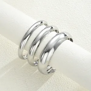 Dettaglio di tre bracciali rigidi in argento lucido su un supporto cilindrico bianco