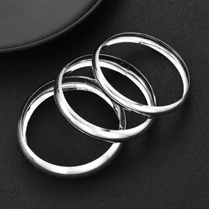 Dettaglio di tre bracciali rigidi argento lucidi sovrapposti con finitura a specchio su nero