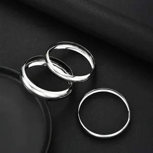 Dettaglio di tre bracciali rigidi in metallo argento lucido su sfondo nero testurizzato