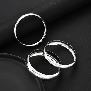 Vista macro di tre bracciali rigidi minimalisti in metallo argento su sfondo scuro