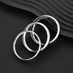 Dettaglio di tre bracciali rigidi minimalisti in argento lucido su uno sfondo scuro