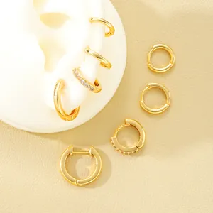 Detalle de pendientes de aro dorados con diamantes sobre un fondo beige texturizado