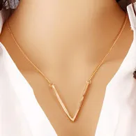 Détail d'un collier avec pendentif en V doré minimaliste porté par un mannequin en chemise