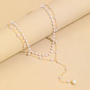 Detailed view of layered gold Y-necklace with elegant faux pearls on a beige stand