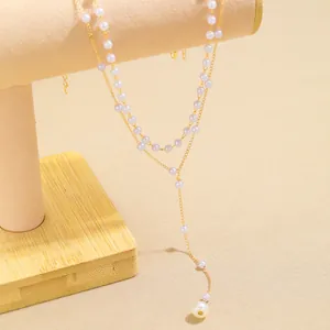 Double-layered gold necklace with faux pearls and Y-shaped tassel on jewelry display stand