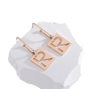 Roségoldene quadratische Ohrhänger mit Buchstaben R Design auf weißem Naturstein