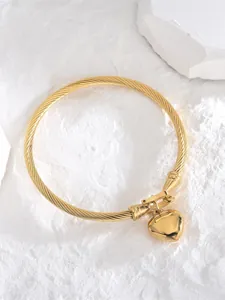 Détail macro du bracelet en fil d'acier torsadé doré avec un charm en cœur poli