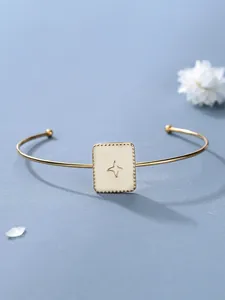 Dettaglio bracciale dorato con quadrato in smalto crema e motivo a stella su blu tenue