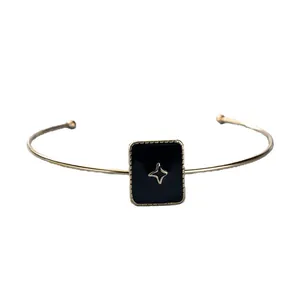 Bracciale rigido dorato con quadrato in smalto nero e stella dorata su sfondo bianco