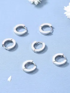 Tre paia di orecchini a cerchio huggie in acciaio inossidabile argento su sfondo blu