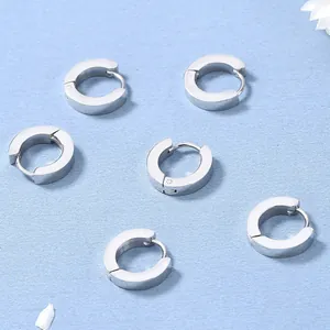 Set di orecchini a cerchio huggie in acciaio lucido su sfondo minimalista blu chiaro
