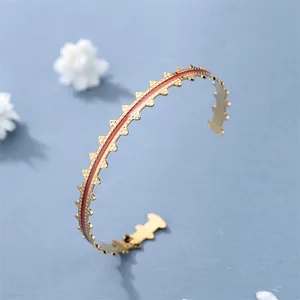 Macro shot of gold-plated bangle featuring red enamel inlay and intricate serrated edges