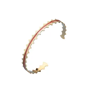 Golden open bangle with red enamel inlay and unique wavy gear-edge design in retro style