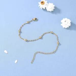 Détail d'un bracelet chaîne en or avec perles sphériques et fermoir mousqueton sur fond bleu