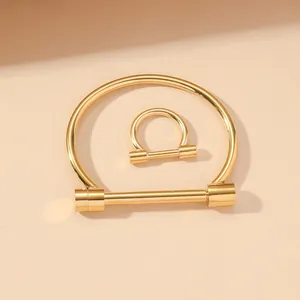 Dettaglio del set bracciale e anello a ferro di cavallo dorato minimalista su sfondo