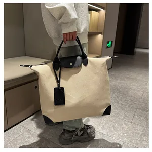 Detail of the beige canvas travel tote featuring black leather handles and logo tag