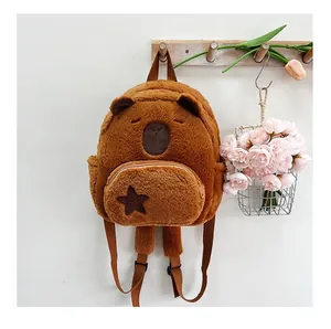 Close-up of plush brown capybara backpack with star patch and zip pocket on a wooden hook