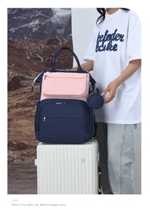 Zaino fasciatoio trapuntato blu navy e rosa con portamonete rotondo su una valigia