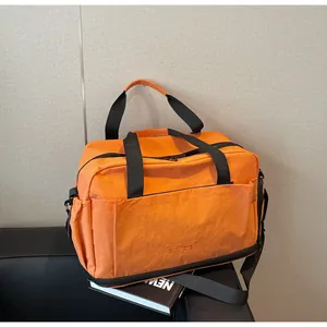 Détail du sac de fitness étanche orange avec poches zippées sur un canapé en cuir noir