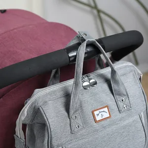 Large capacity light gray diaper bag backpack hanging on a stroller handle with metal clips